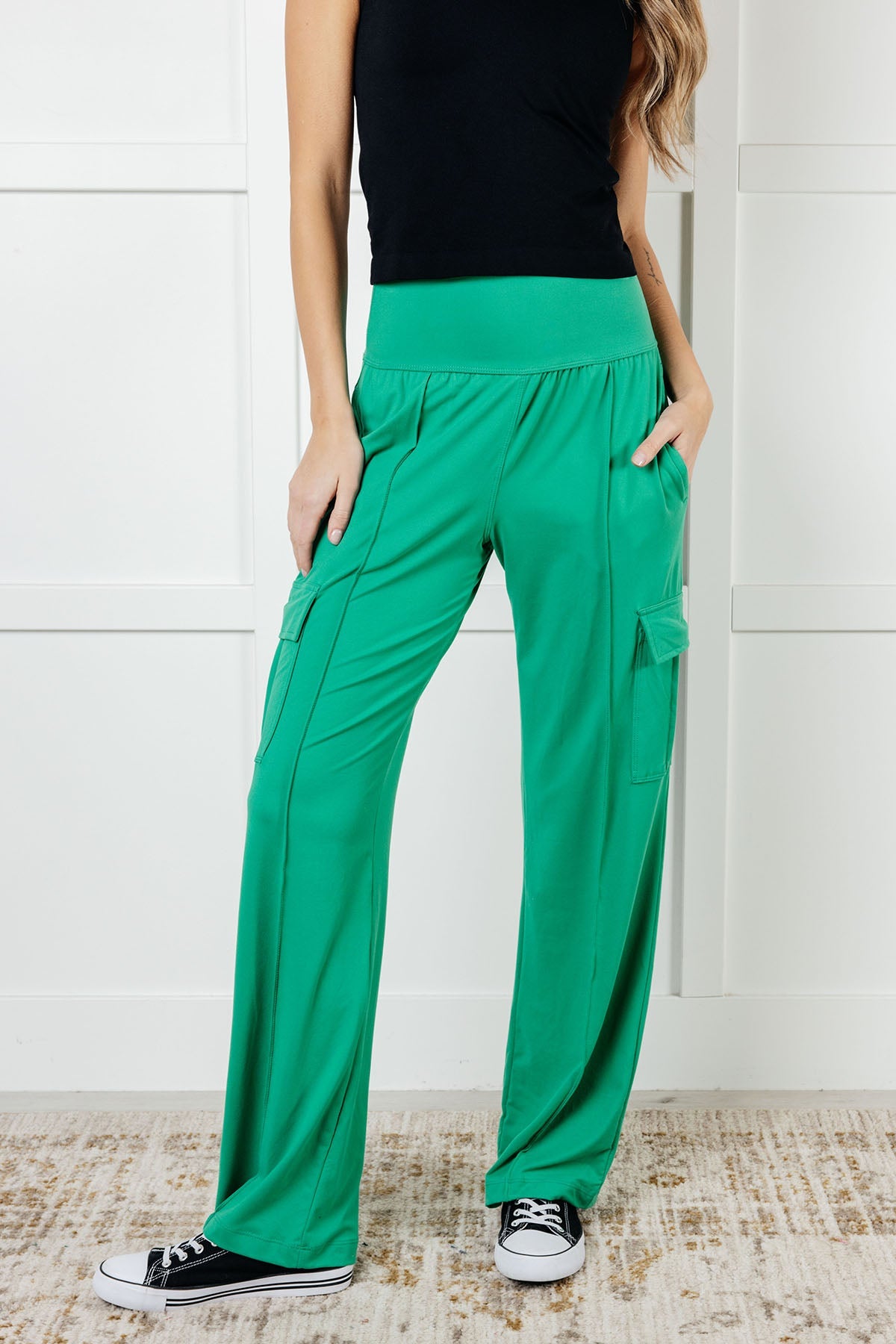 A person standing wearing emerald green straight-leg cargo pants with a drawstring waistband and functional side pockets, paired with a black top and black sneakers.