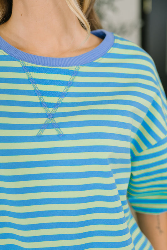 Close-up of a person wearing a short-sleeve crewneck top with horizontal light green and medium blue stripes, plus a light blue ribbed collar.