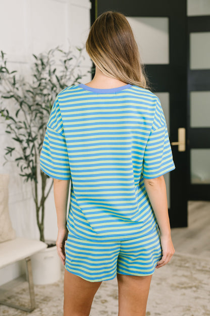 A woman viewed from behind wearing a matching short-sleeve striped pajama set in turquoise and white, featuring a crew neck and shorts.