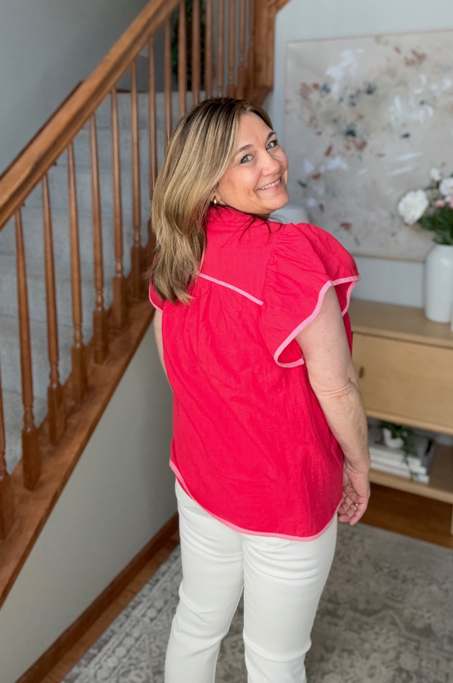 Woman wearing a red jacket standing in a home interior with a staircase and decor.