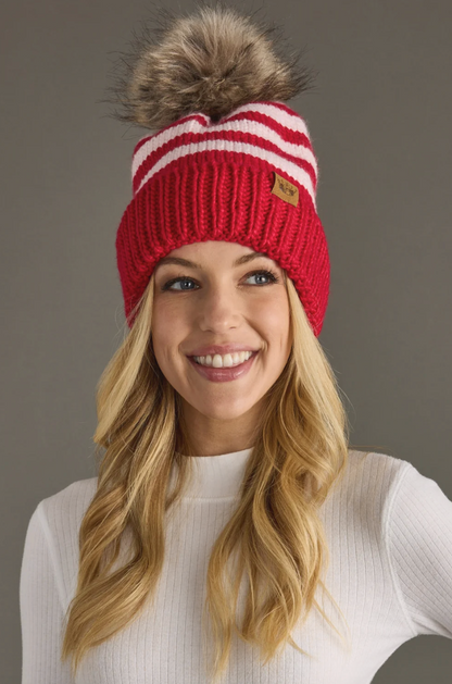 Woman wearing a red and white striped knit beanie with a fur pom-pom against a gray background