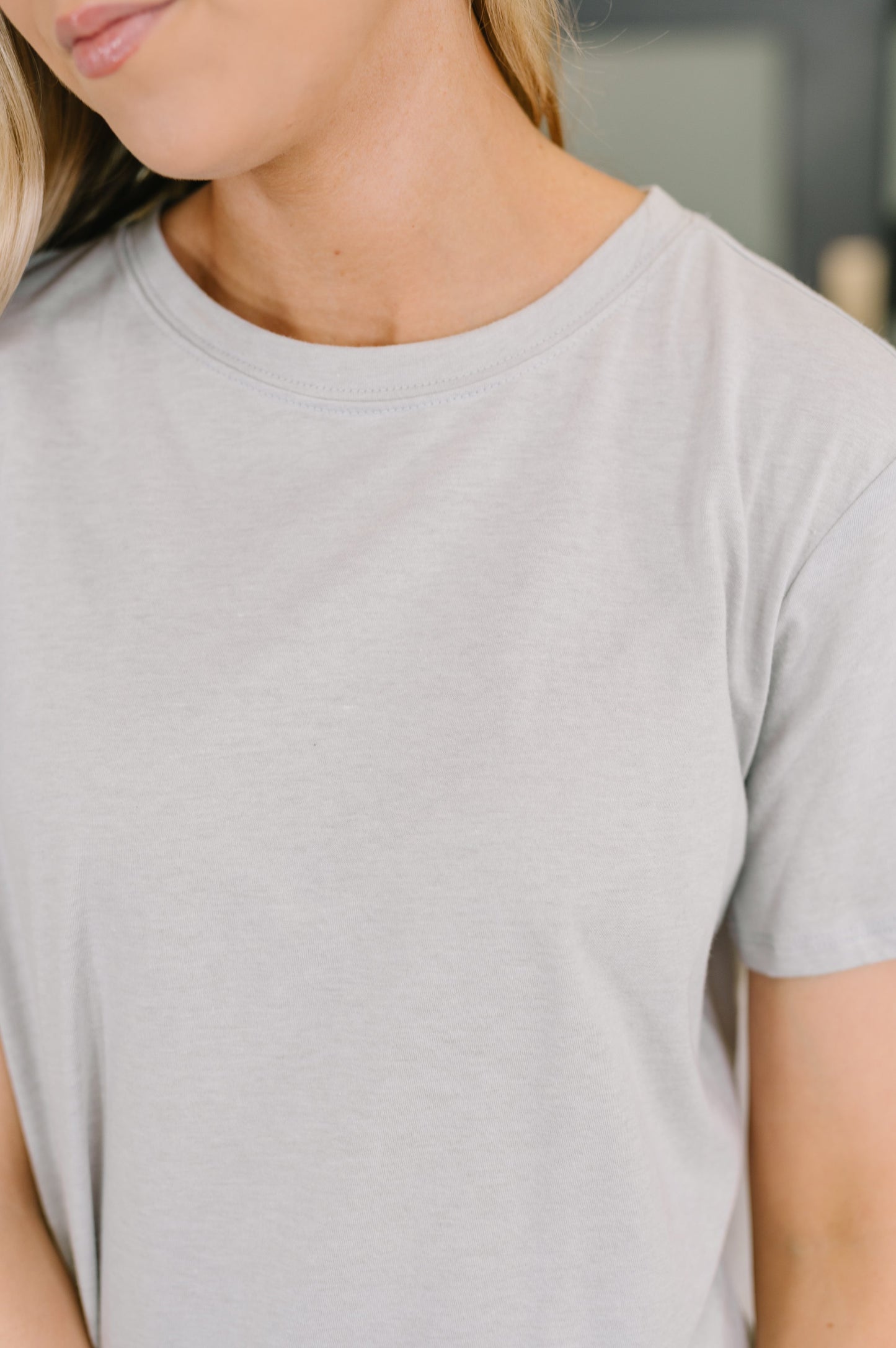 Person wearing a plain light gray t-shirt with a blurred background