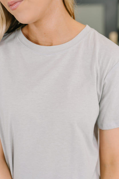 Person wearing a plain light gray t-shirt with a blurred background