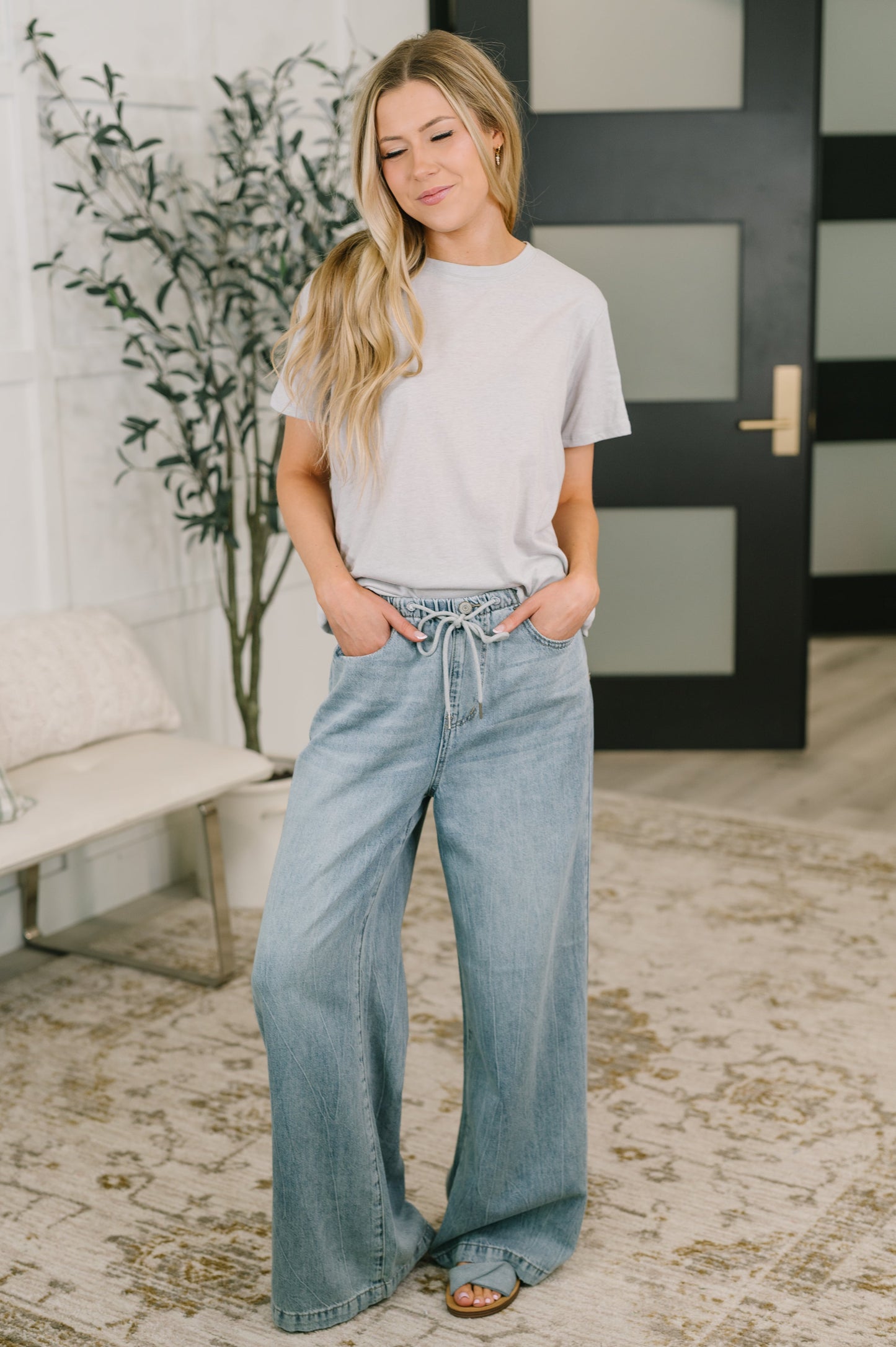 Woman wearing a light gray t-shirt and blue jeans in an indoor setting.