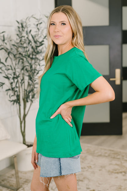 Woman wearing a green t-shirt and denim shorts standing indoors.