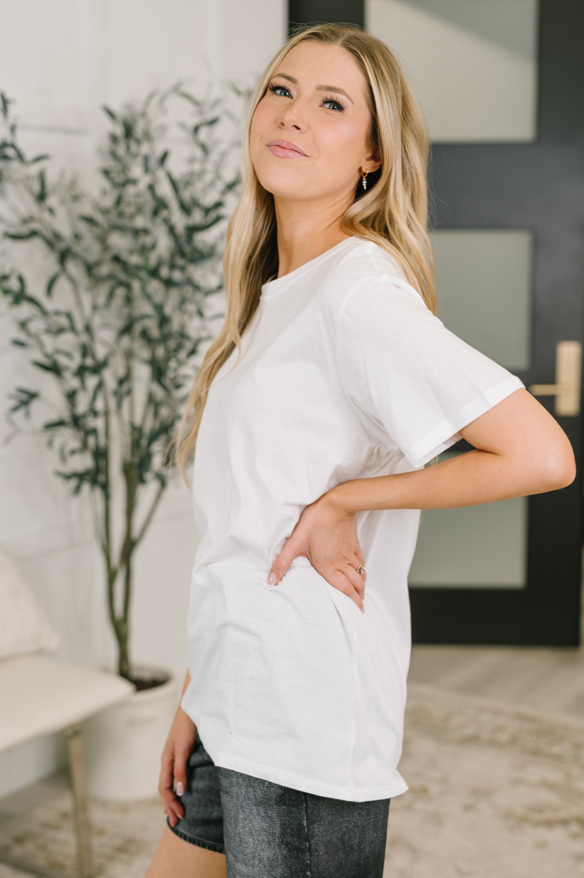 Woman wearing a white t-shirt in an indoor setting with a plant and furniture in the background