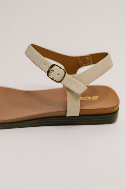 Beige sandal with a brown sole on a light gray background