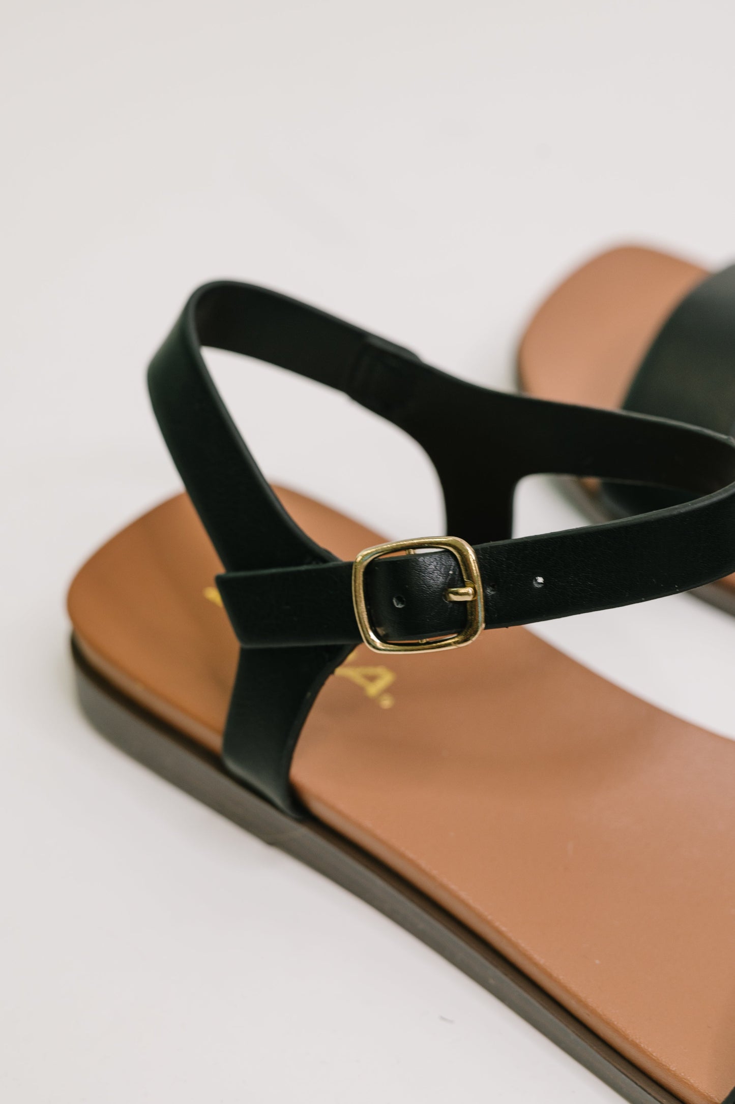 Black sandal with a gold buckle on a white background