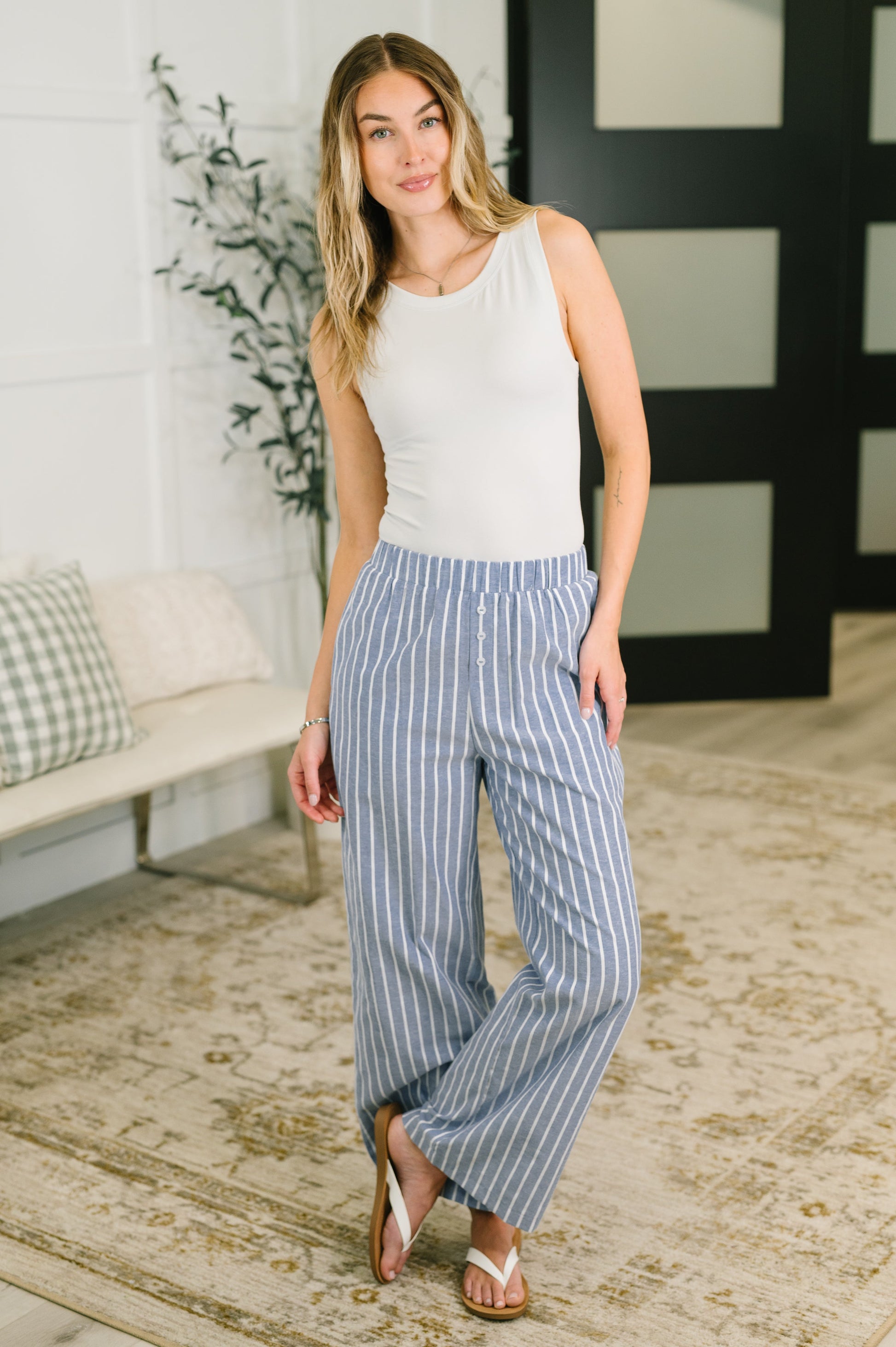 Woman wearing a white sleeveless top and blue striped pants in an indoor setting.