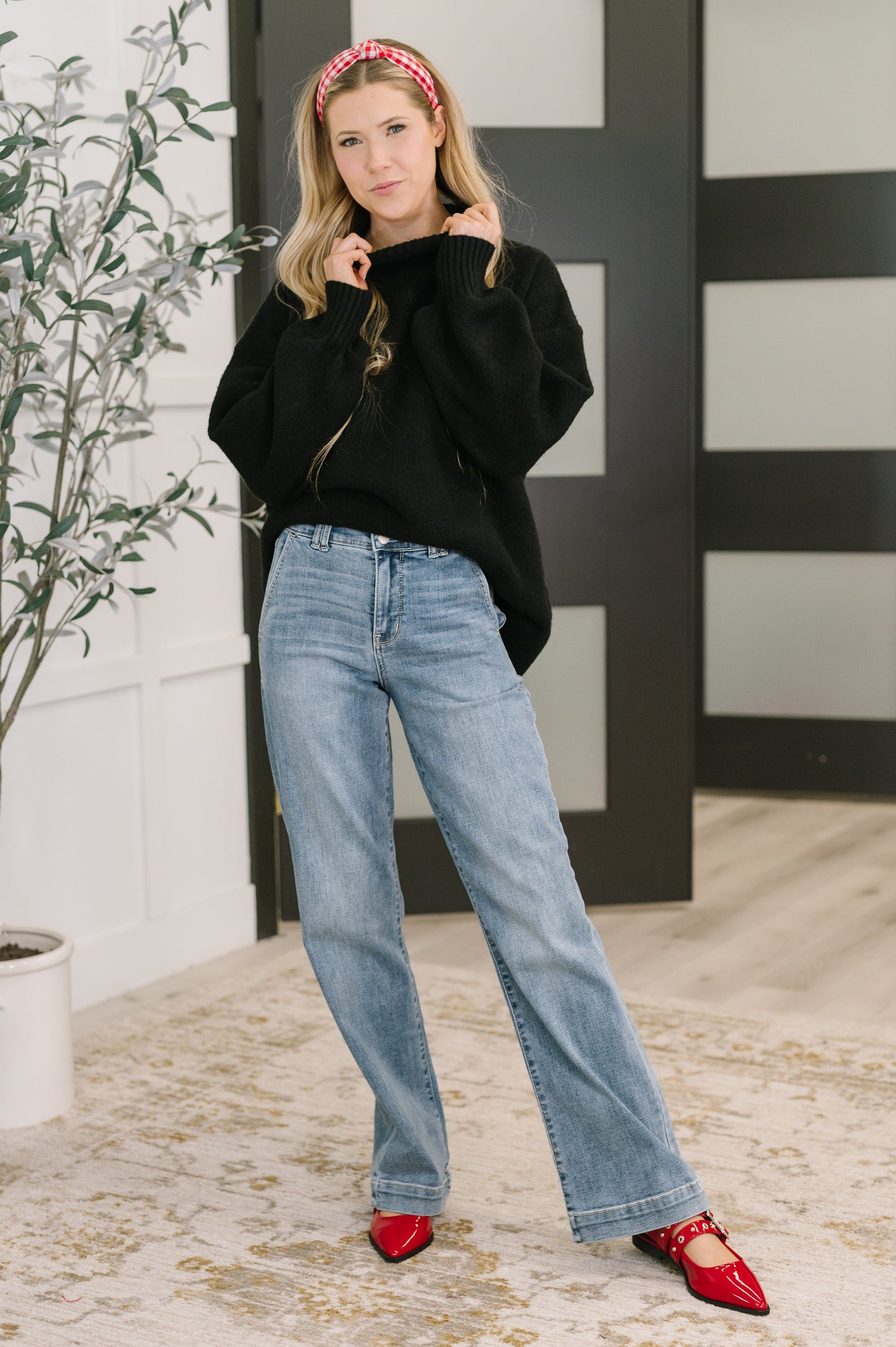 Woman wearing a black sweater, blue jeans, and red shoes in an indoor setting.