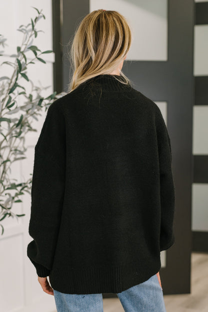 Person wearing a black sweater in an indoor setting with a plant and striped wall.