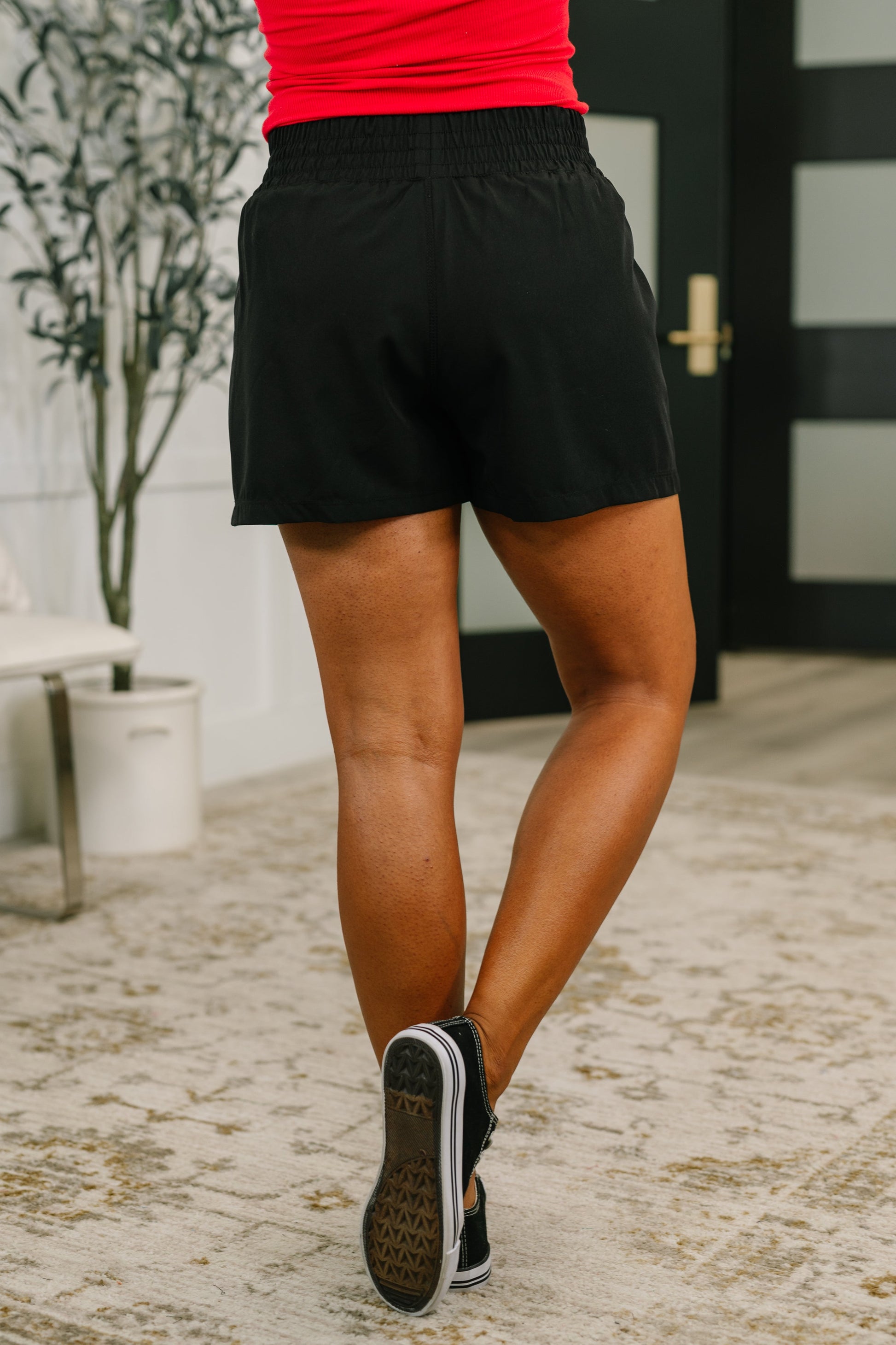 Person wearing black shorts and a red top, standing on a textured floor.