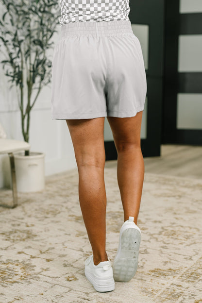 Person wearing light gray shorts and white sneakers on a stone path.
