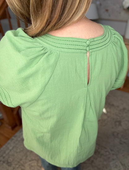 Green top worn by a person, with a blurred background