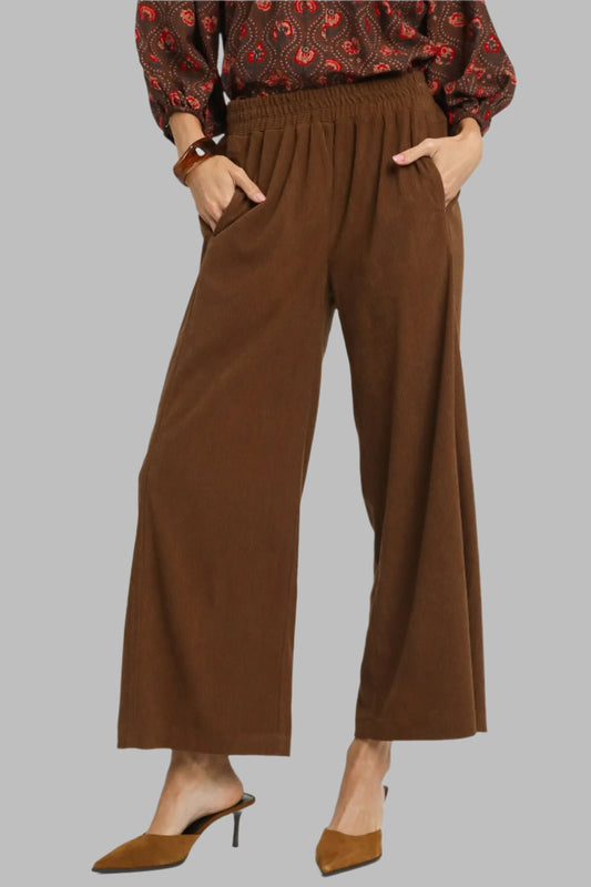 Brown wide-leg pants worn with a patterned top on a white background