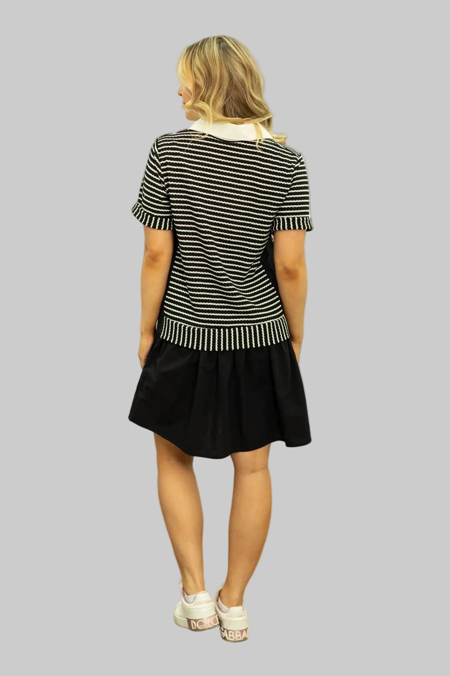 Woman wearing a black and white striped top and black skirt against a white wall.