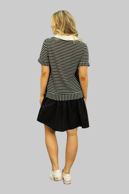 Woman wearing a black and white striped top and black skirt against a white wall.