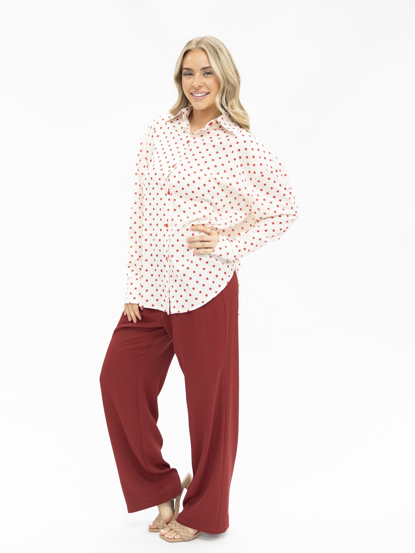Woman wearing a white blouse with red patterns and red pants on a white background