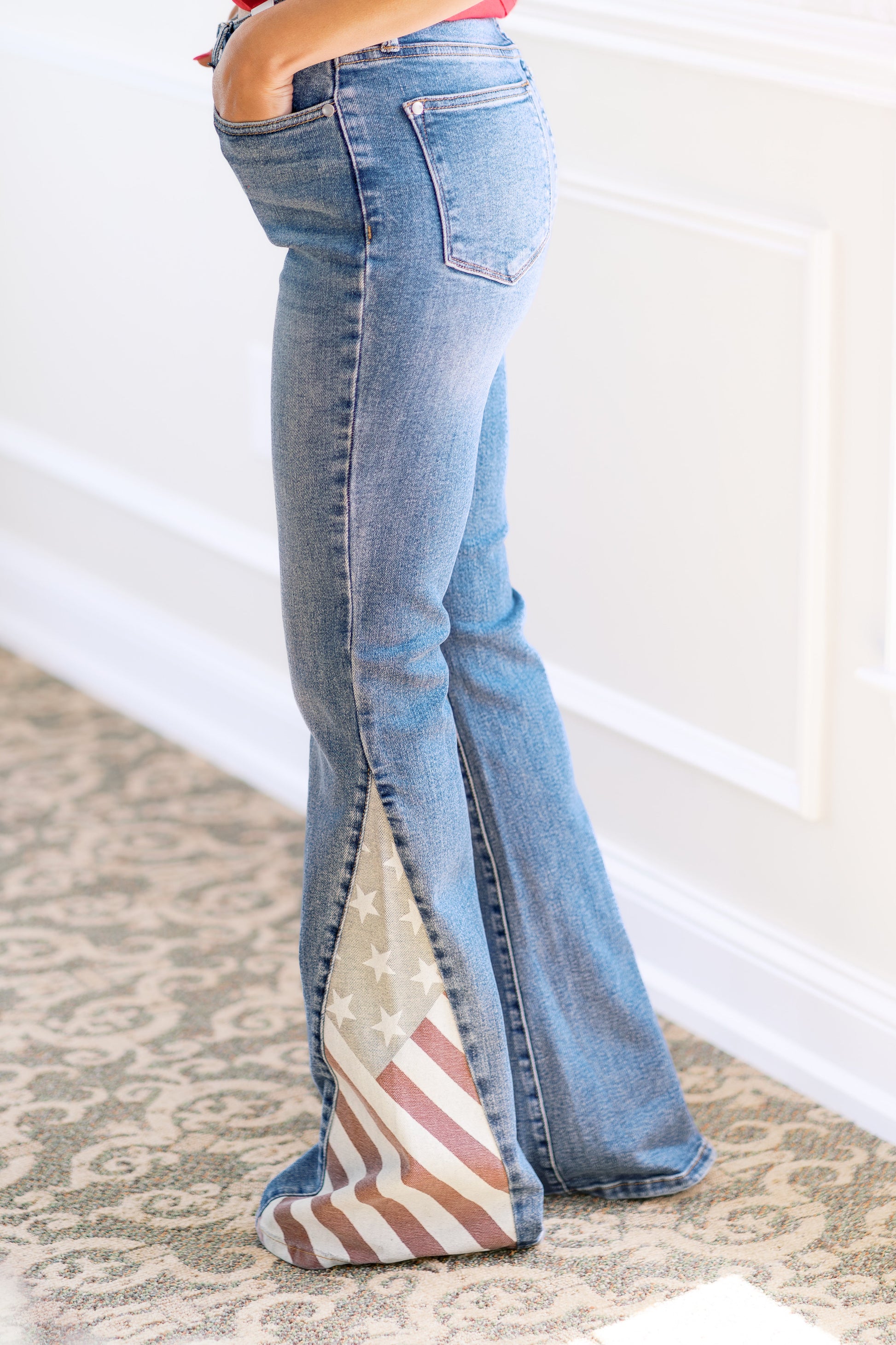 Flared jeans with American flag pattern on a carpeted floor.