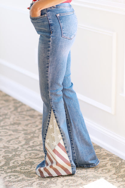 Flared jeans with American flag pattern on a carpeted floor.