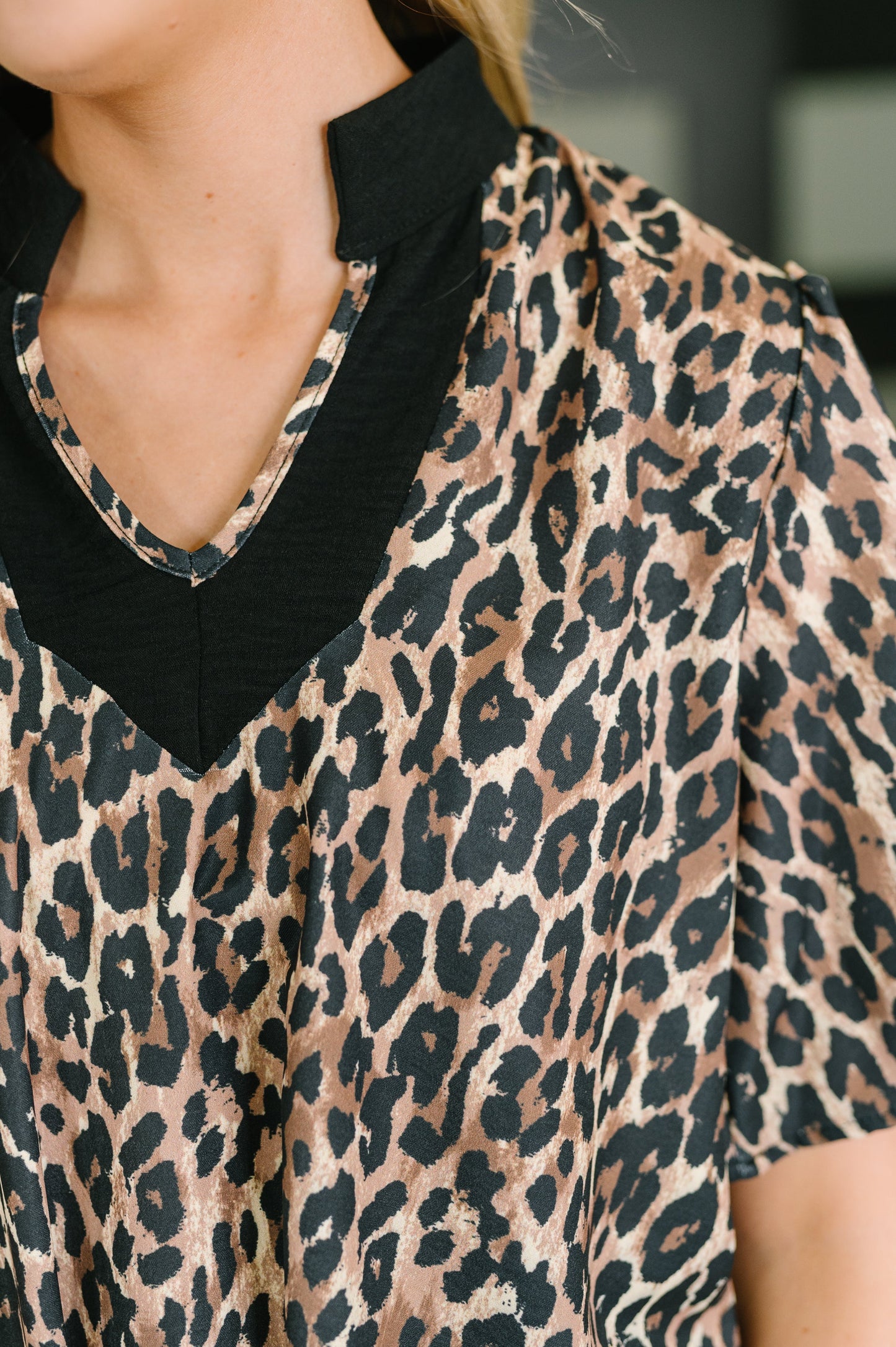 Close-up of a leopard print blouse with a black V-neck collar and short sleeves, worn by a model.