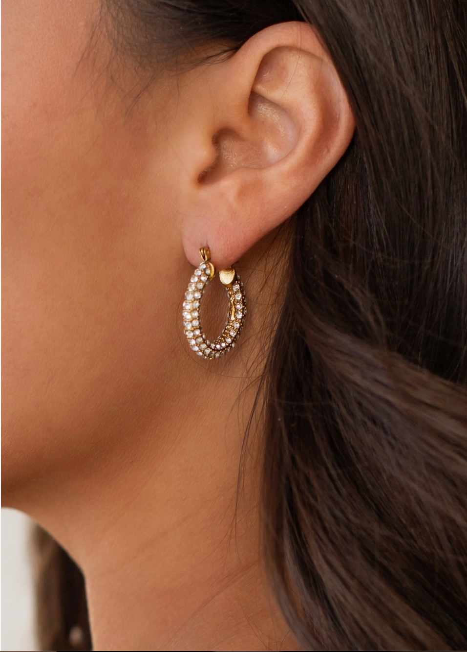Close-up of an ear wearing a gold hoop earring with small stones.