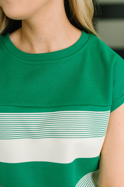 Close-up of a person wearing a green short-sleeve top with a wide white horizontal stripe and thin green horizontal stripes across the chest.