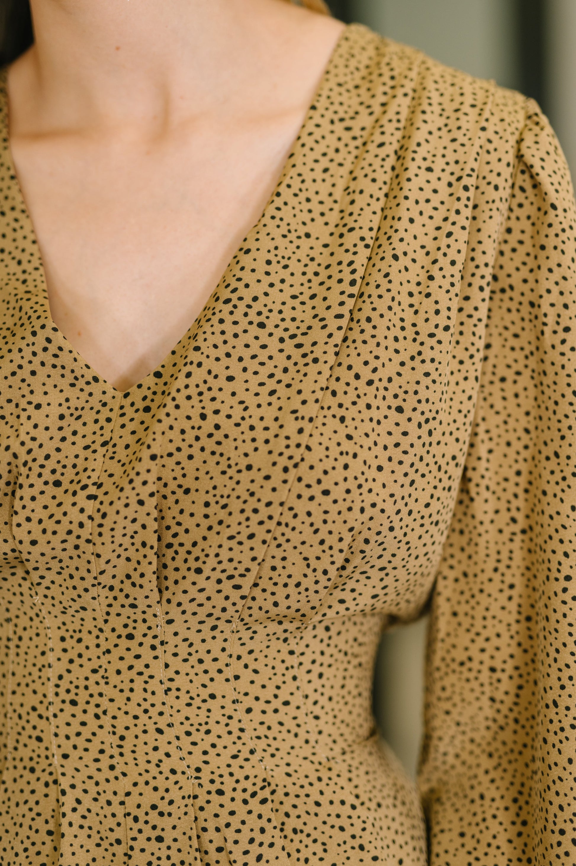 Close-up of a person wearing a beige blouse with black dot pattern