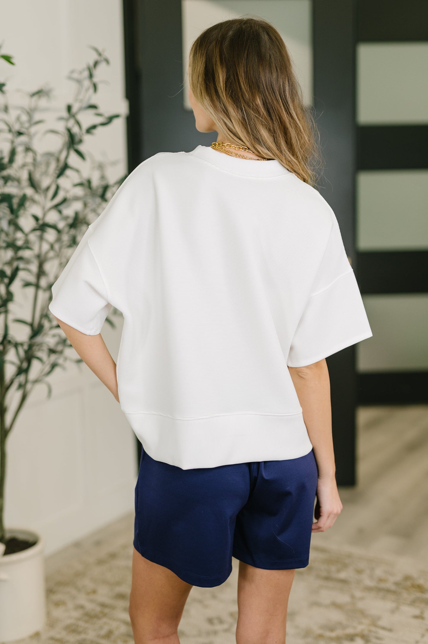 Person wearing a white oversized shirt and navy shorts in an indoor setting.