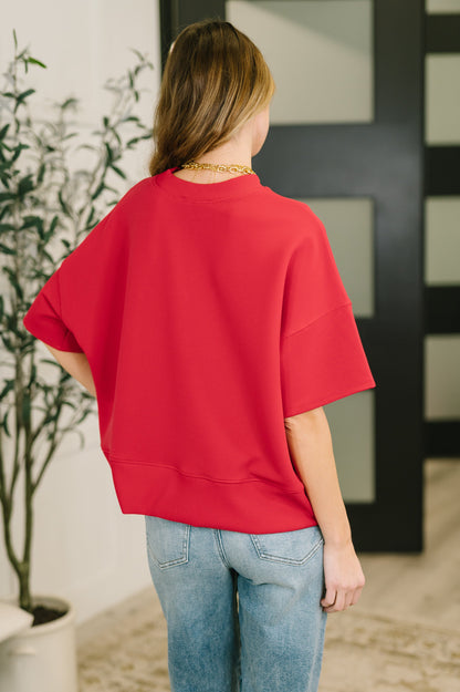 Person wearing a red oversized shirt and blue jeans standing indoors.