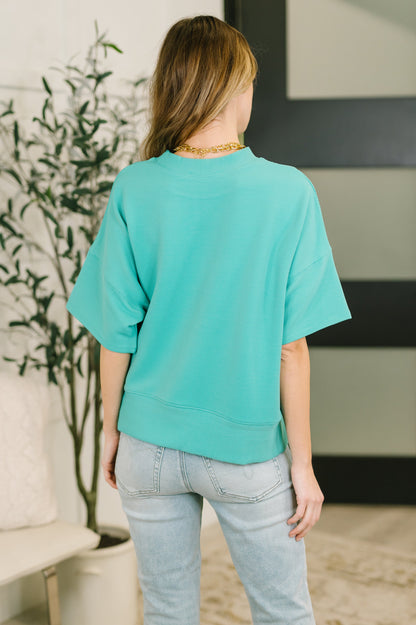 Person wearing a teal oversized shirt and light blue jeans in an indoor setting.