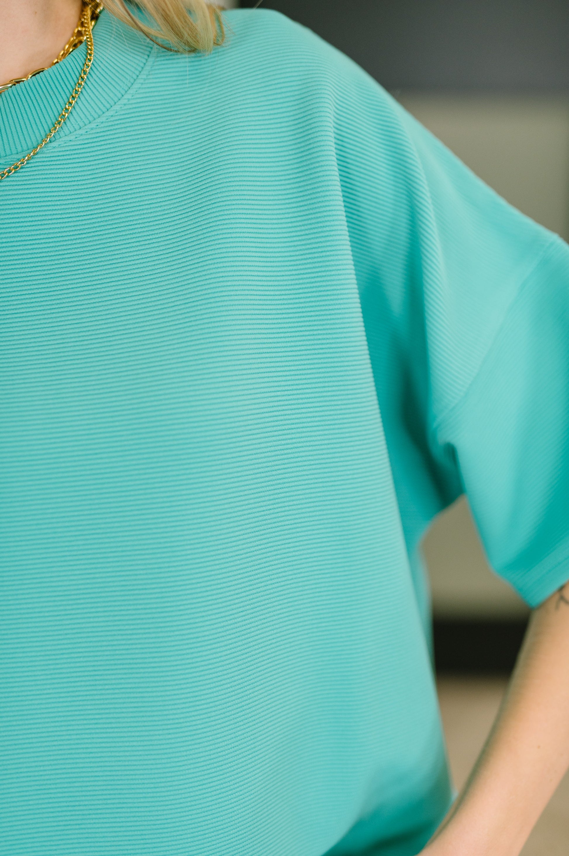 Close-up of a person wearing a teal sweater with a blurred background