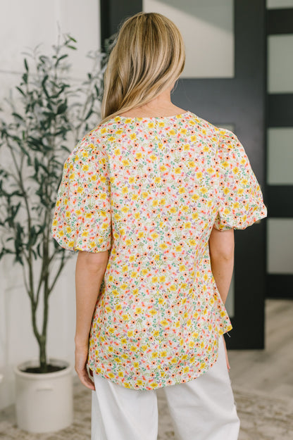 Person wearing a colorful floral blouse in an indoor setting with a plant and wall art.