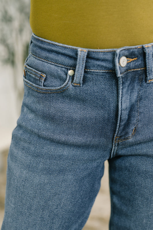 Close-up of a person wearing medium-wash blue denim jeans with a ribbed olive green top visible at the waist.