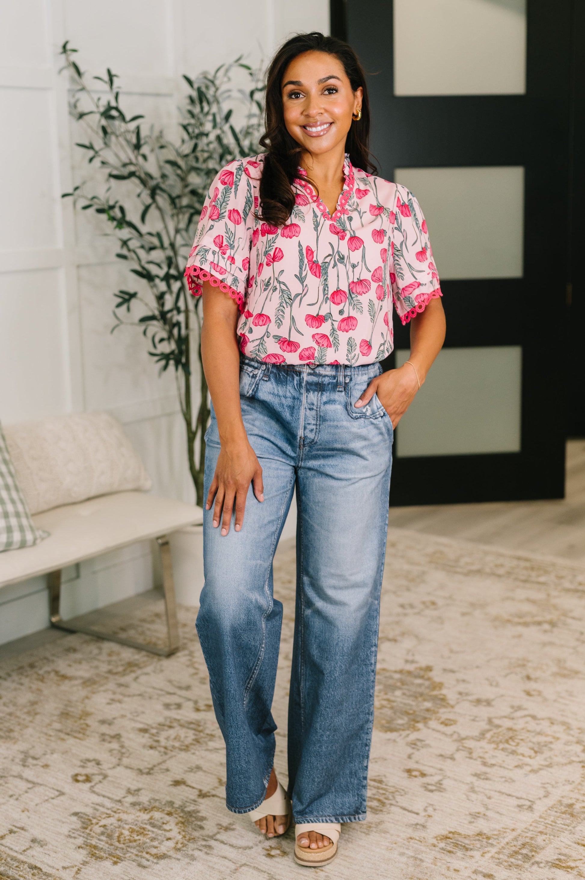 Woman wearing a pink floral blouse and blue jeans standing indoors.