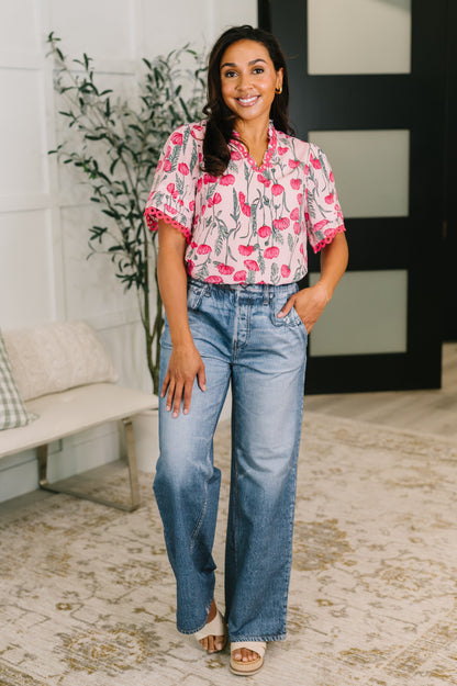 Woman wearing a pink floral blouse and blue jeans standing indoors.