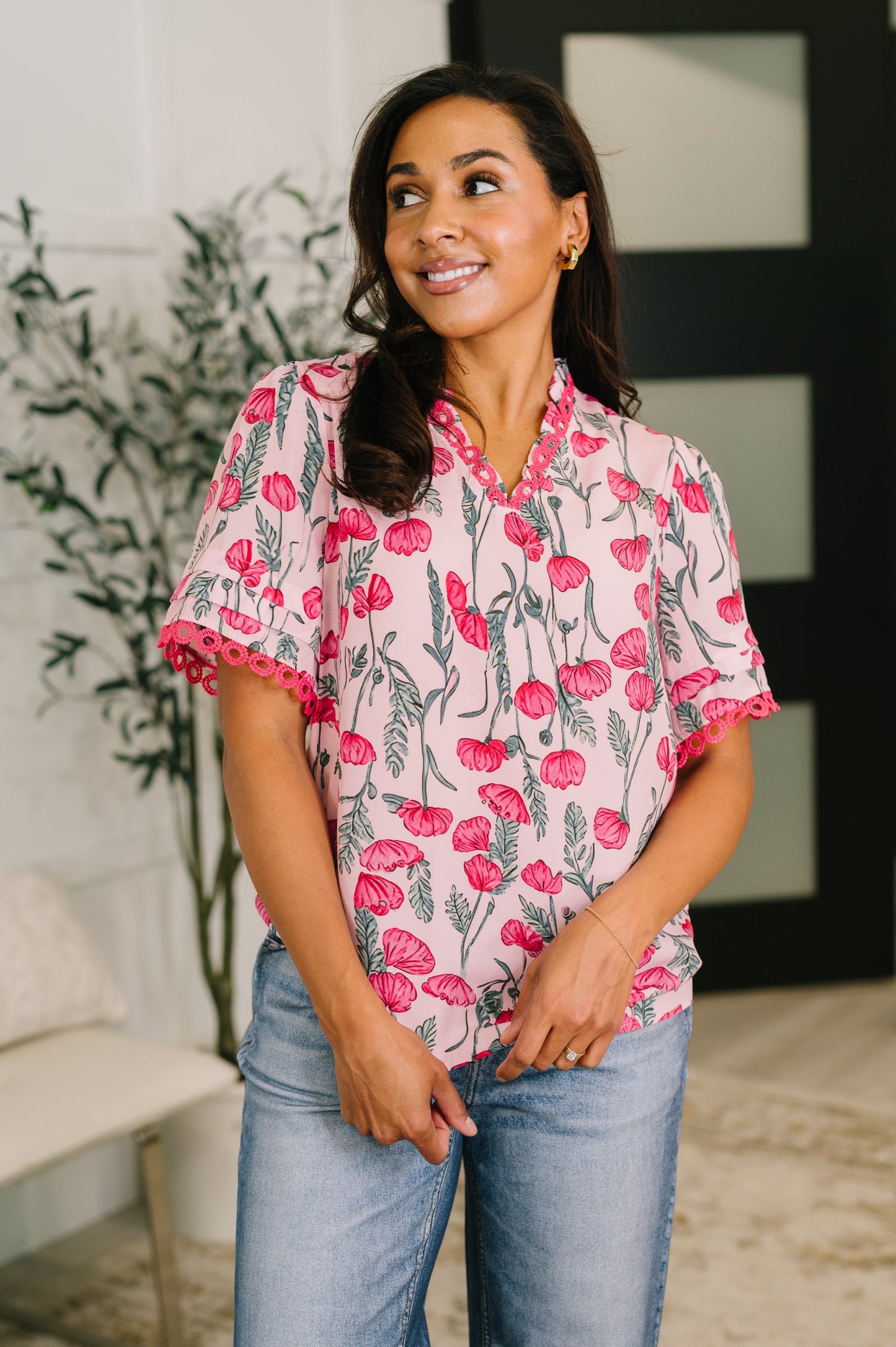 Woman wearing a floral blouse with pink and red flowers indoors.