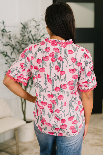 Woman wearing a floral blouse with pink flowers and green leaves in an indoor setting.