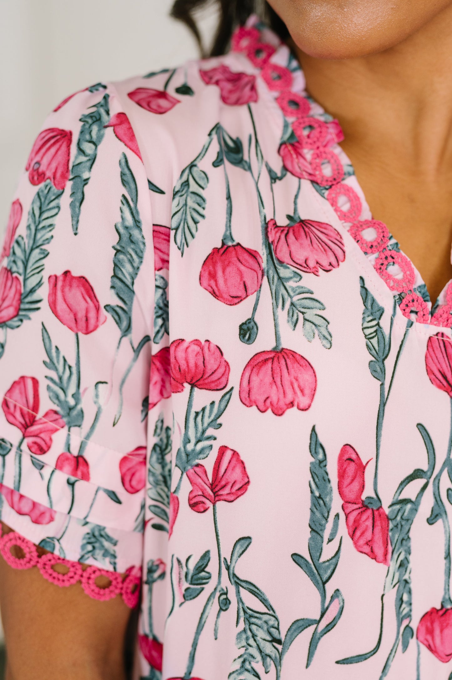 Close-up of a floral dress with pink flowers and green leaves on a light pink background.