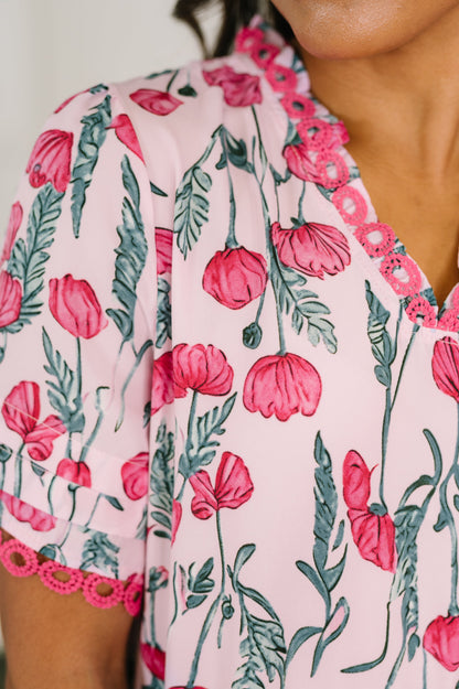 Close-up of a floral dress with pink flowers and green leaves on a light pink background.