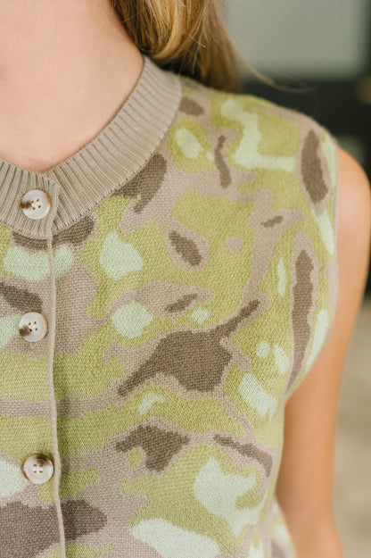 Close-up of a sleeveless knit top with a muted camouflage pattern in olive green, beige, and brown, featuring a ribbed crew neck and front buttons.