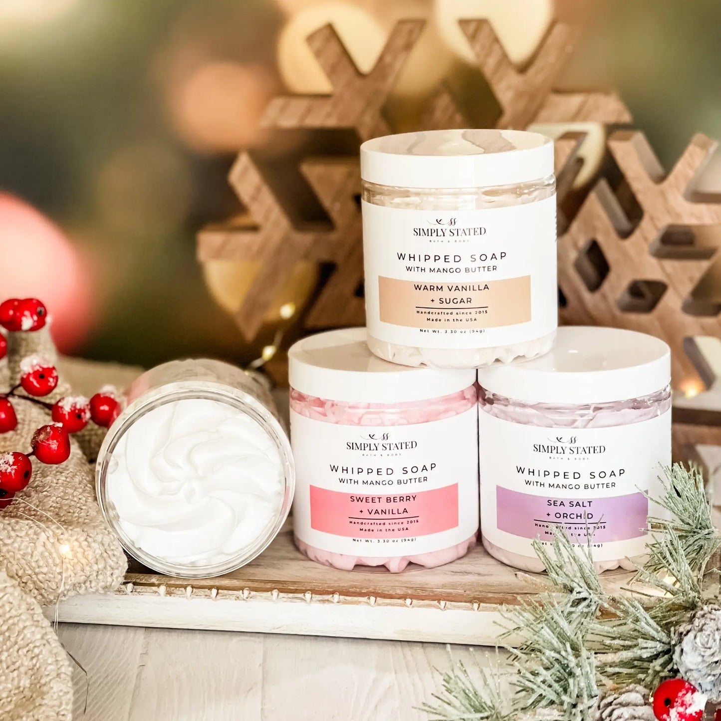 Three containers of whipped soap with decorative Christmas elements in the background