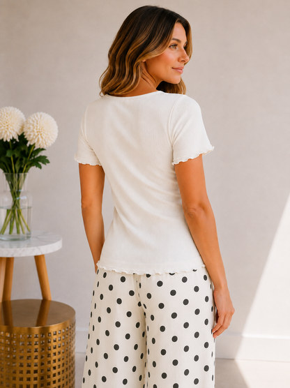 Woman wearing a white top and polka dot pants in a minimal indoor setting.