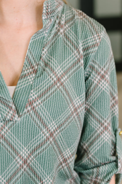 Close-up of a person wearing a green plaid shirt with white and brown intersecting stripes, showing the collar and upper chest area.
