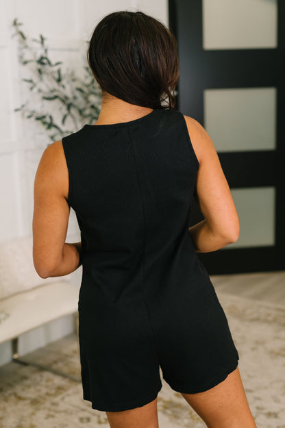 Person wearing a black sleeveless romper in an indoor setting.