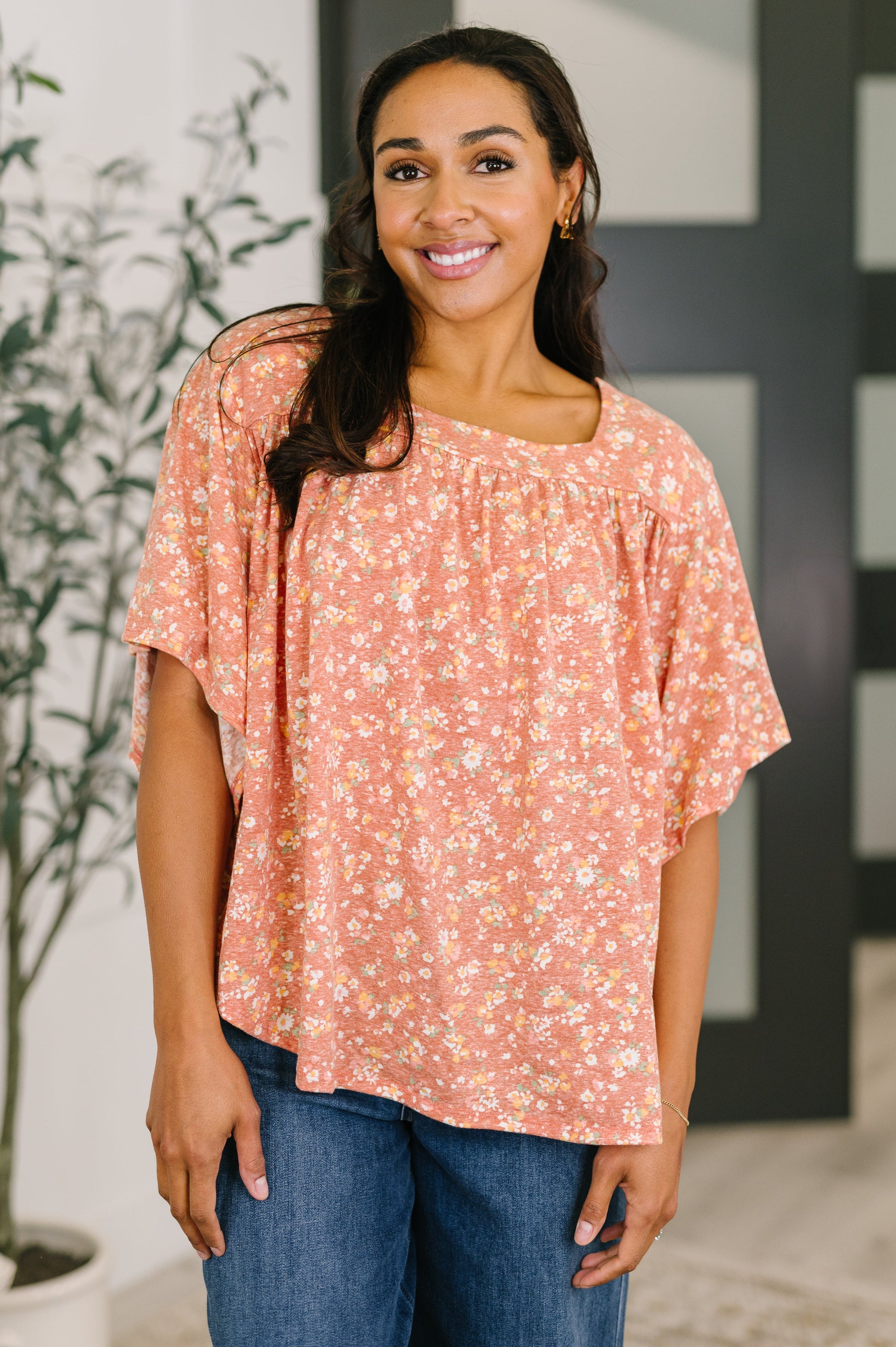 Woman wearing a floral blouse and jeans indoors with a plant in the background