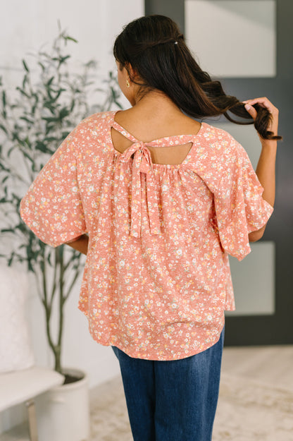 Woman wearing a pink floral blouse with a blurred indoor background