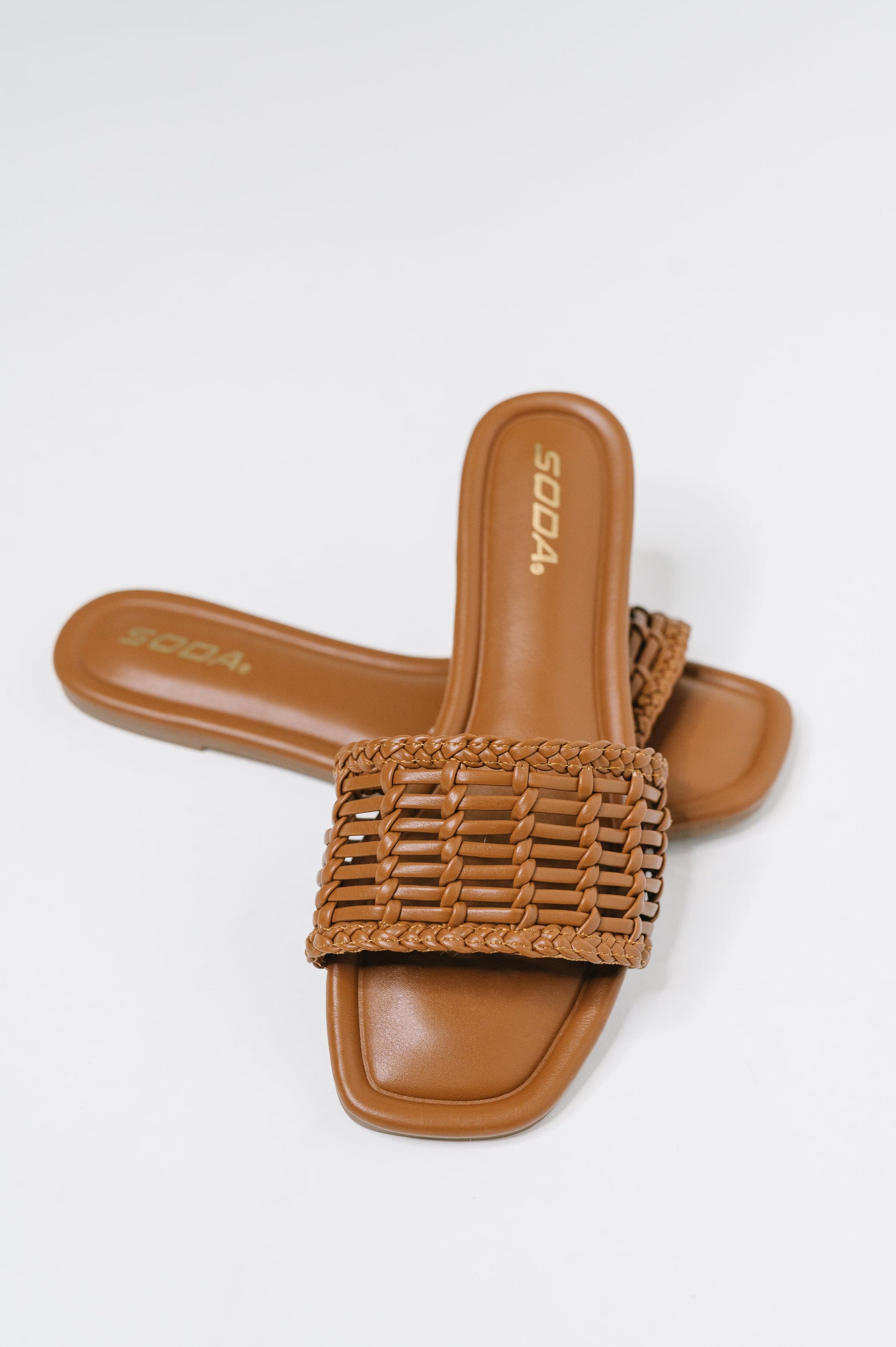 A pair of tan slide sandals with a woven strap, shown on a light gray background. The brand name 'SODA' is visible on the insole.