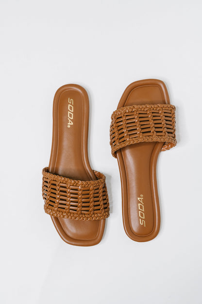 A pair of brown woven slide sandals with a flat sole, shown from a top-down view on a light gray background. The brand name 'SODA' is printed in gold on the footbed.