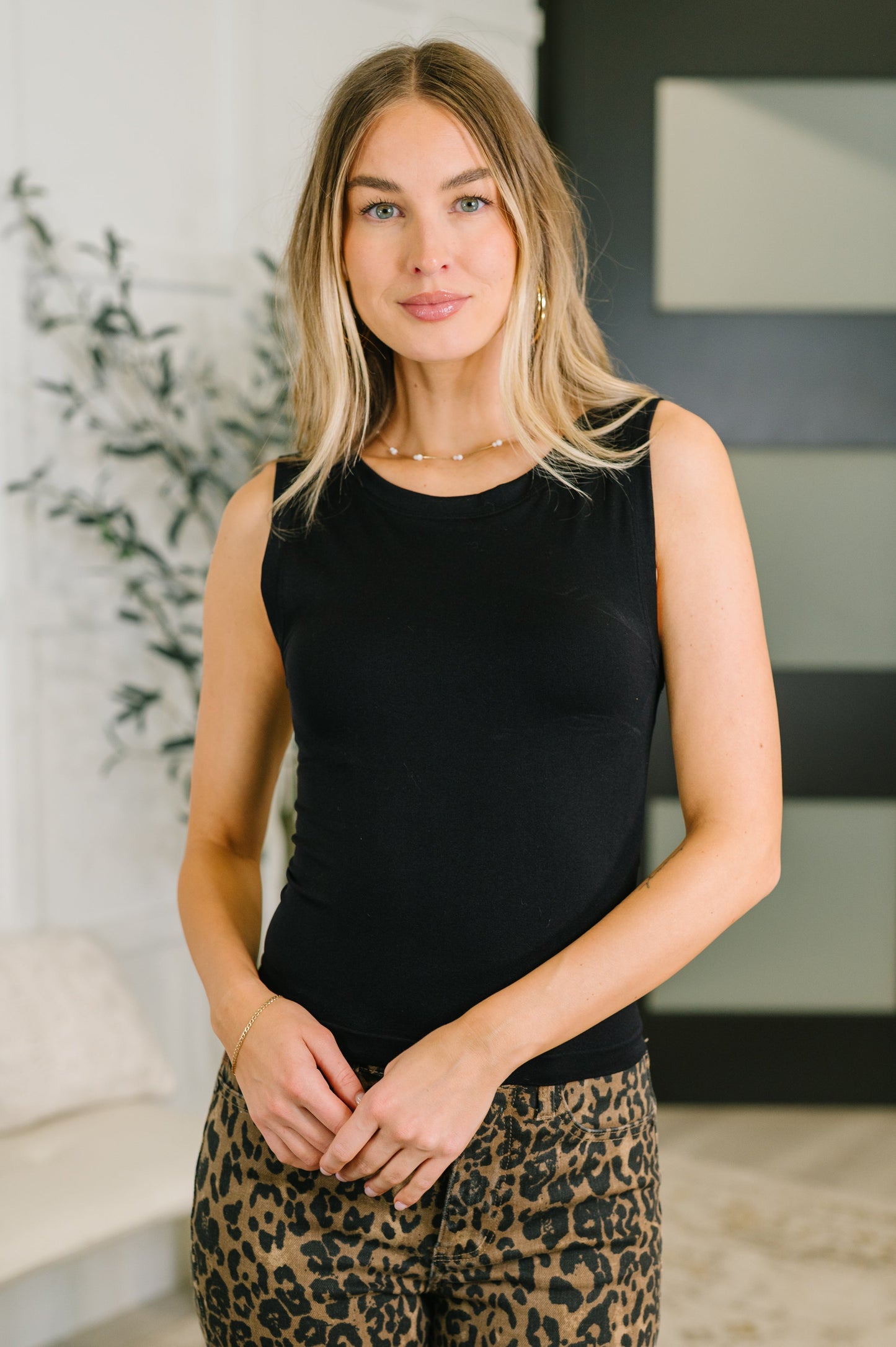 Woman wearing a black sleeveless top and leopard print pants indoors.